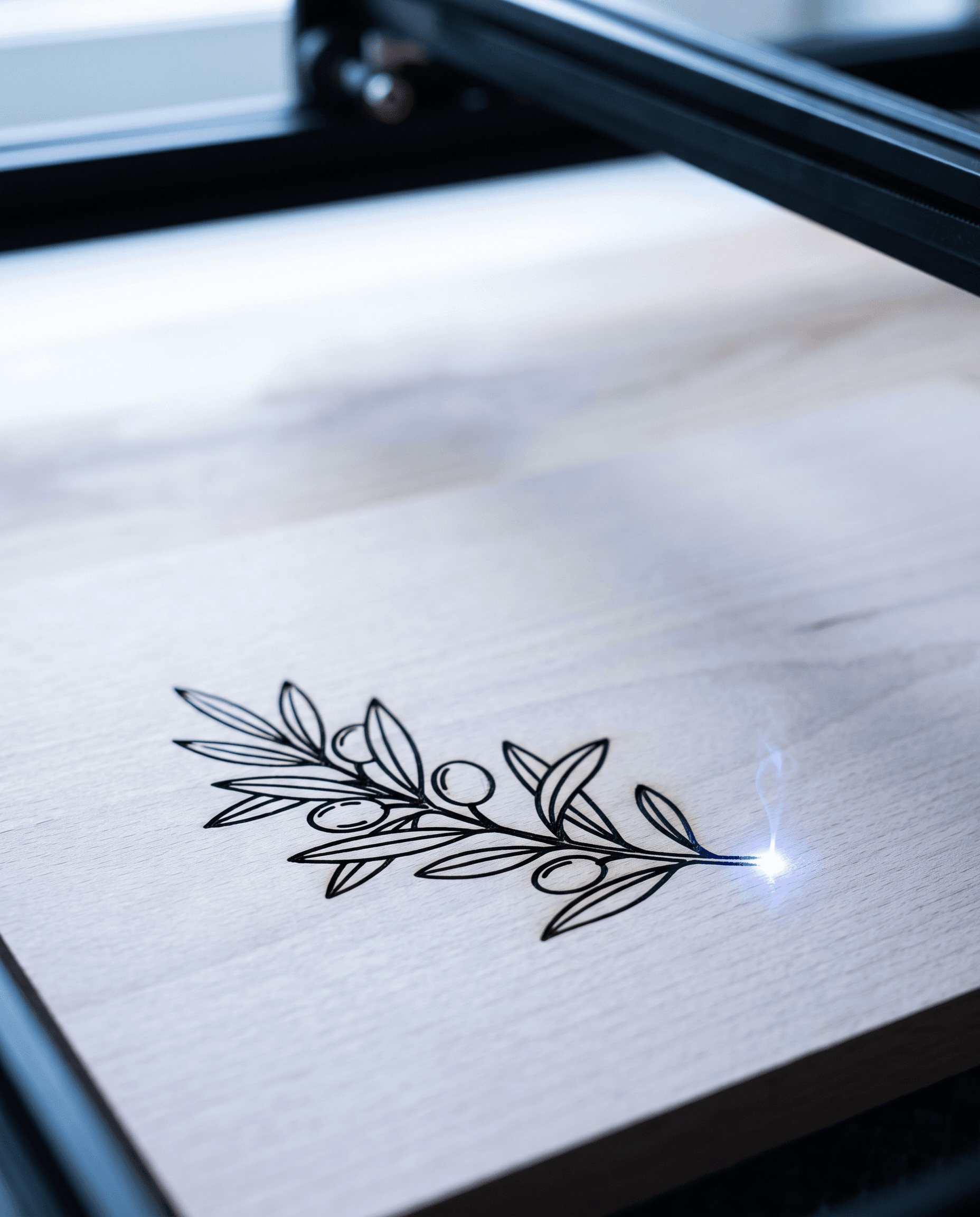 Laserpunkt graviert einen Zweig mit schmalen Blättern als dunkle Linie in eine helle Holzplatte, Nahaufnahme